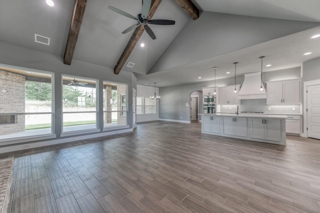 unfurnished living room featuring beam ceiling, ceiling fan with notable chandelier, and high vaulted ceiling