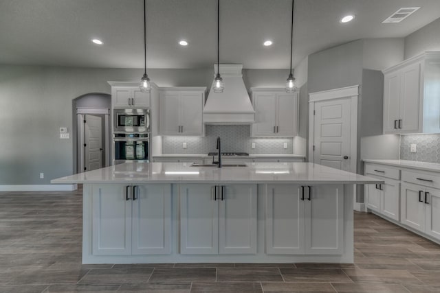 kitchen with white cabinets, stainless steel appliances, hanging light fixtures, and an island with sink