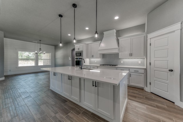 kitchen with an inviting chandelier, white cabinets, hanging light fixtures, custom range hood, and stainless steel appliances