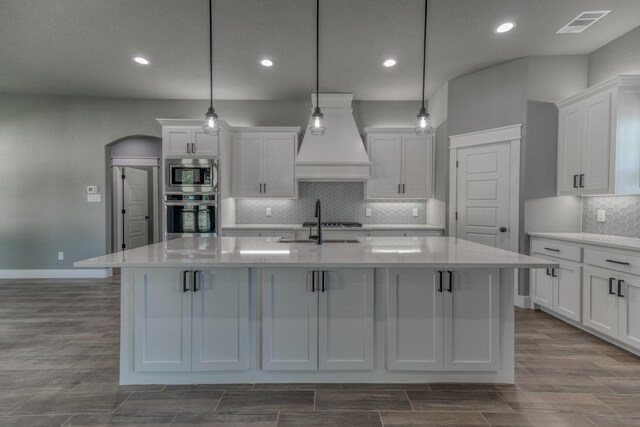 kitchen with stainless steel appliances, custom exhaust hood, a sink, white cabinetry, and recessed lighting