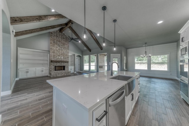 kitchen featuring white cabinetry, stainless steel appliances, a brick fireplace, decorative light fixtures, and a kitchen island with sink