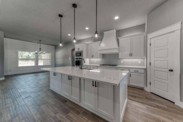 kitchen with custom exhaust hood, appliances with stainless steel finishes, white cabinetry, a chandelier, and wood tiled floors