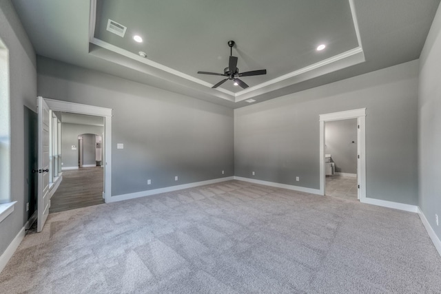 unfurnished bedroom with crown molding, ceiling fan, connected bathroom, a tray ceiling, and light colored carpet