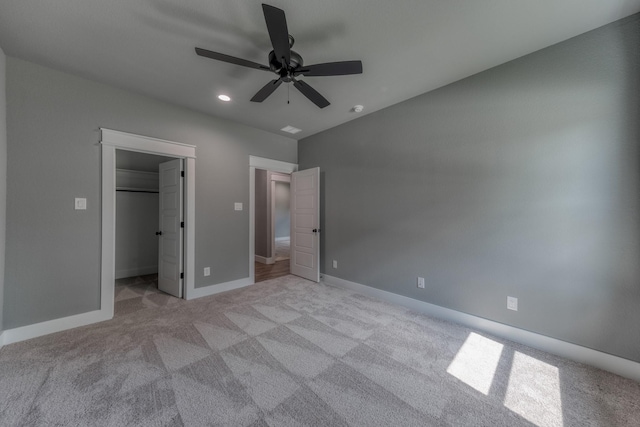 unfurnished bedroom with a closet, a spacious closet, ceiling fan, and light colored carpet