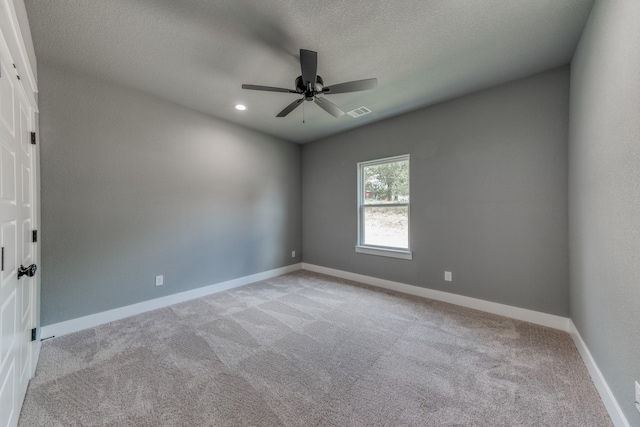 spare room with a textured ceiling, light colored carpet, and ceiling fan