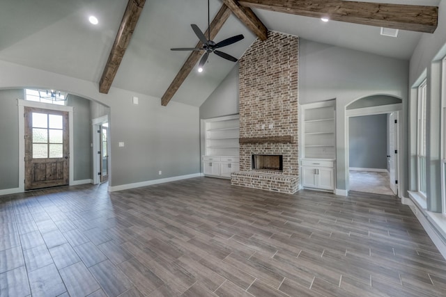 unfurnished living room featuring a brick fireplace, high vaulted ceiling, built in features, and ceiling fan