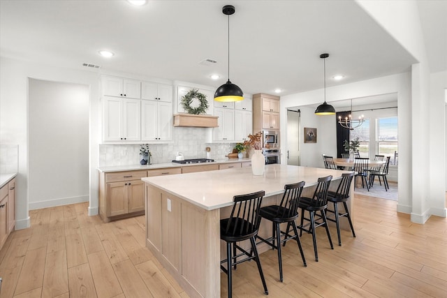 kitchen with a spacious island, hanging light fixtures, tasteful backsplash, light brown cabinetry, and appliances with stainless steel finishes