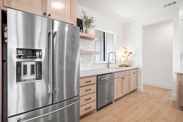 kitchen featuring sink, light brown cabinets, tasteful backsplash, light hardwood / wood-style floors, and appliances with stainless steel finishes