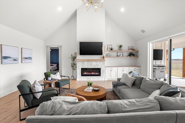 living room with a chandelier, a fireplace, high vaulted ceiling, and light hardwood / wood-style flooring