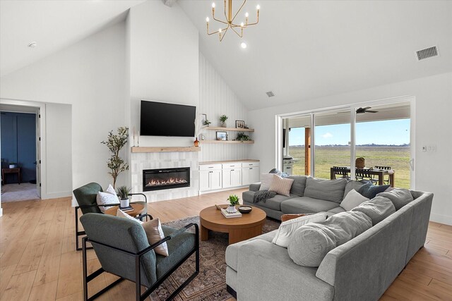 living room with beam ceiling, light hardwood / wood-style flooring, high vaulted ceiling, a fireplace, and ceiling fan with notable chandelier