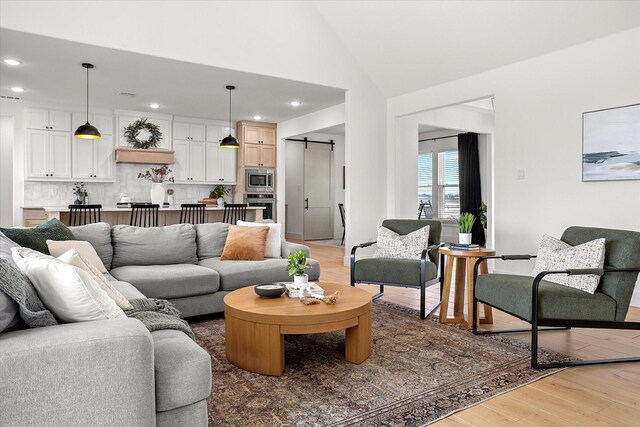 living room featuring a barn door, high vaulted ceiling, and light wood-type flooring