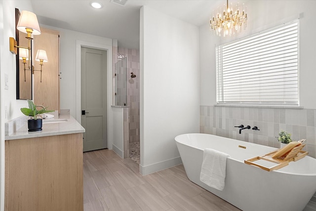 bathroom with a notable chandelier, vanity, shower with separate bathtub, and tile walls