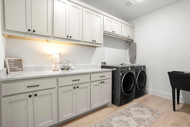 washroom with washing machine and clothes dryer, cabinets, and light wood-type flooring