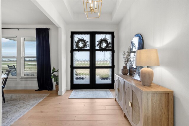 entrance foyer featuring a raised ceiling, french doors, light hardwood / wood-style flooring, and a notable chandelier