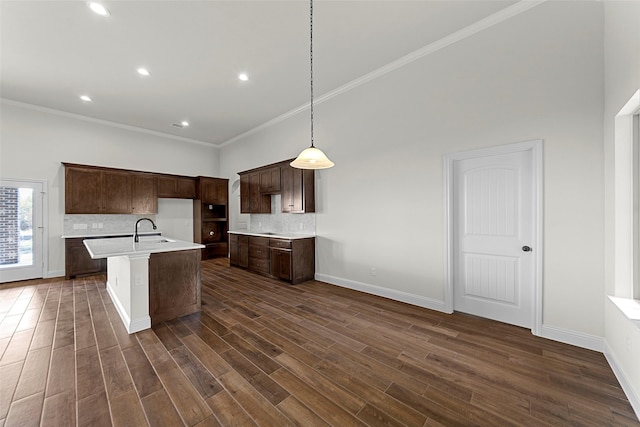 kitchen featuring backsplash, a center island with sink, pendant lighting, and ornamental molding