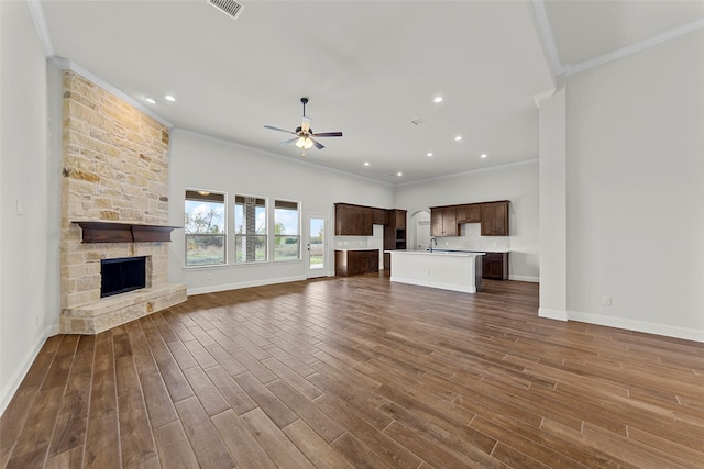 unfurnished living room with ceiling fan, crown molding, dark wood-type flooring, sink, and a stone fireplace