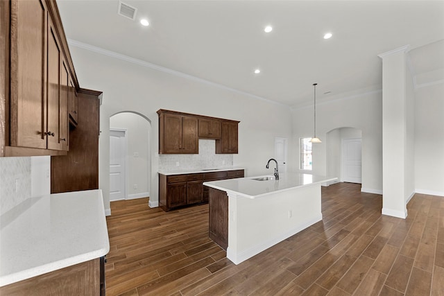 kitchen with pendant lighting, a kitchen island with sink, ornamental molding, and sink