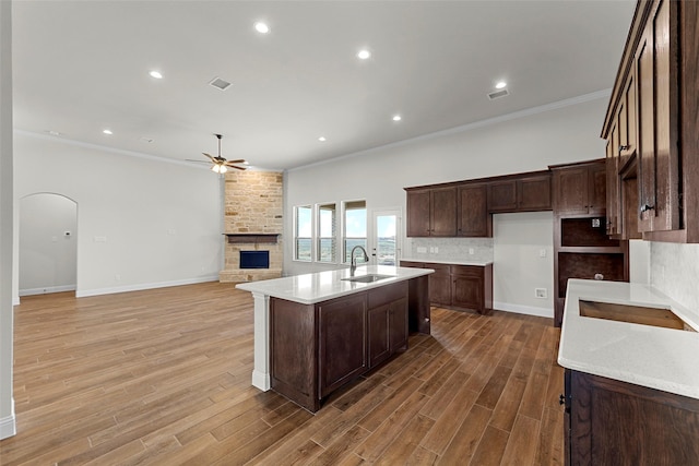 kitchen with sink, hardwood / wood-style flooring, dark brown cabinets, an island with sink, and a stone fireplace