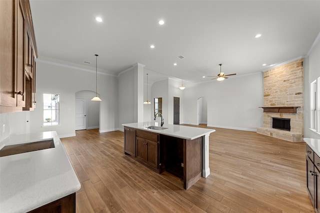 kitchen featuring sink, a kitchen island with sink, pendant lighting, a fireplace, and light hardwood / wood-style floors