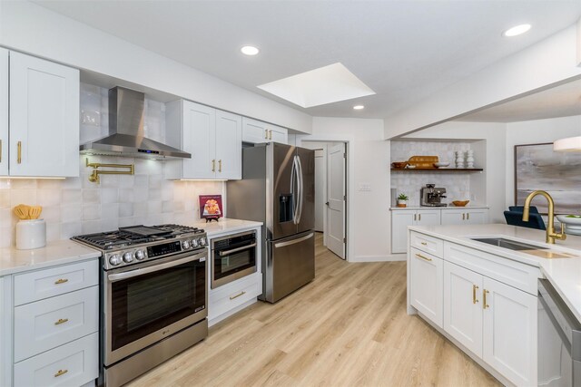 kitchen featuring white cabinets, a skylight, wall chimney exhaust hood, appliances with stainless steel finishes, and tasteful backsplash