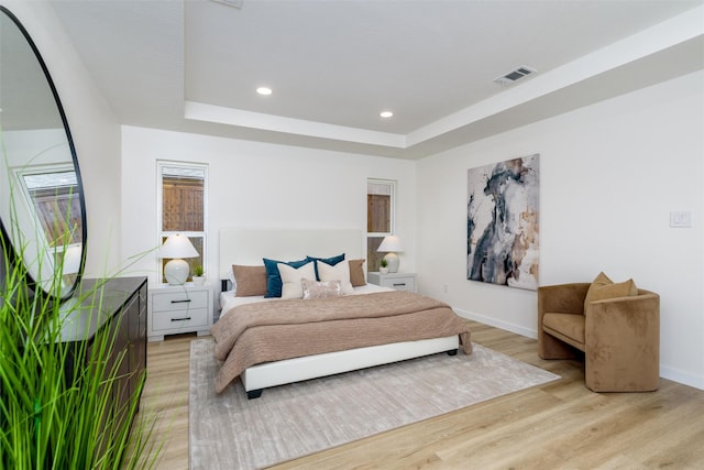 bedroom with a raised ceiling and light wood-type flooring