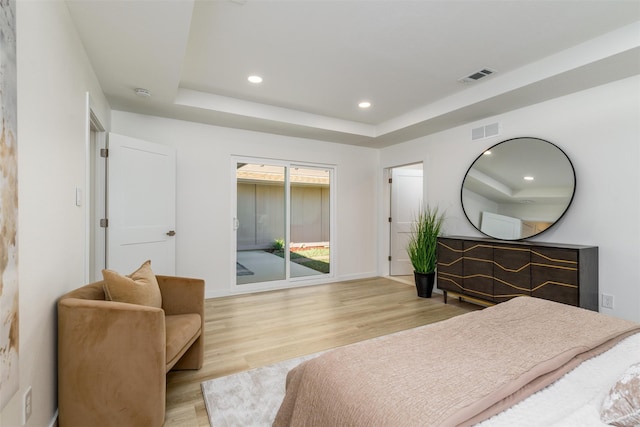 bedroom with a tray ceiling, light hardwood / wood-style flooring, and access to outside