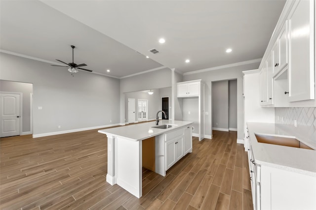 kitchen featuring an island with sink, sink, white cabinets, backsplash, and light hardwood / wood-style flooring