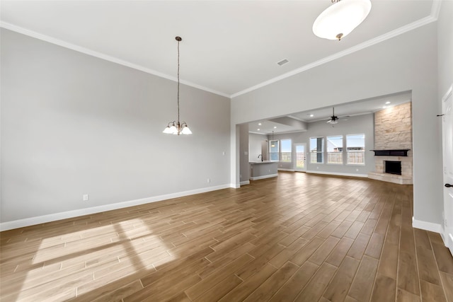 unfurnished living room with wood-type flooring, ornamental molding, ceiling fan with notable chandelier, and a fireplace