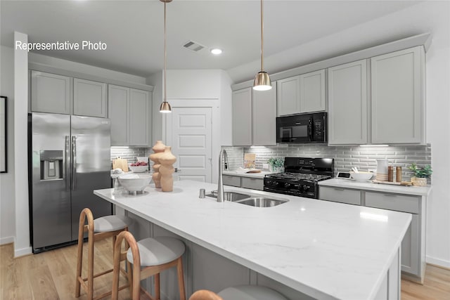 kitchen with decorative backsplash, light stone counters, sink, black appliances, and hanging light fixtures