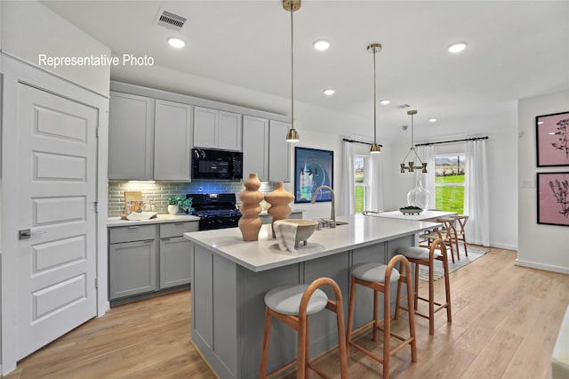 kitchen featuring tasteful backsplash, an island with sink, decorative light fixtures, gray cabinets, and black appliances