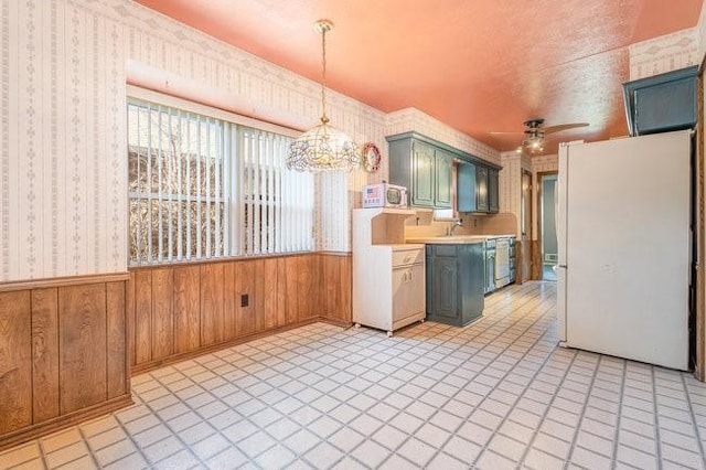 kitchen featuring ceiling fan with notable chandelier, wood walls, sink, white fridge, and green cabinets