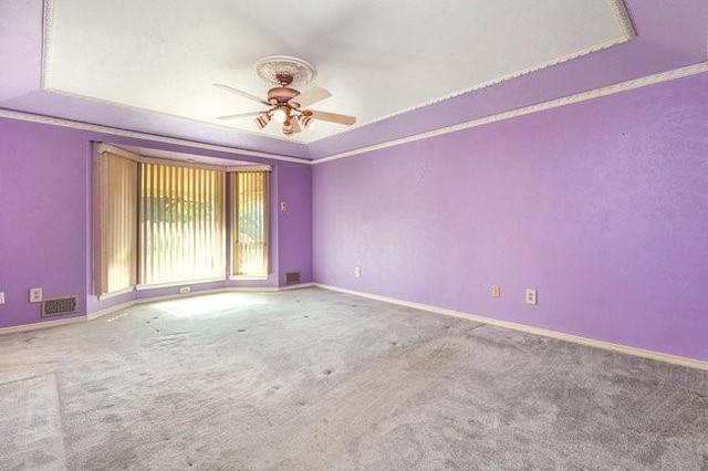 carpeted empty room with a raised ceiling, ornamental molding, and ceiling fan