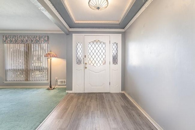 foyer entrance featuring hardwood / wood-style flooring, ornamental molding, and a raised ceiling