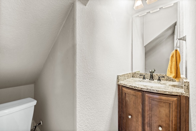 bathroom featuring vanity, toilet, and lofted ceiling