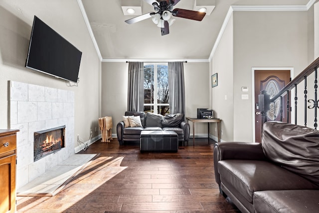 living room with ceiling fan, a fireplace, ornamental molding, and dark wood-type flooring