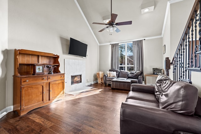 living room featuring dark hardwood / wood-style flooring, ornamental molding, ceiling fan, high vaulted ceiling, and a tiled fireplace