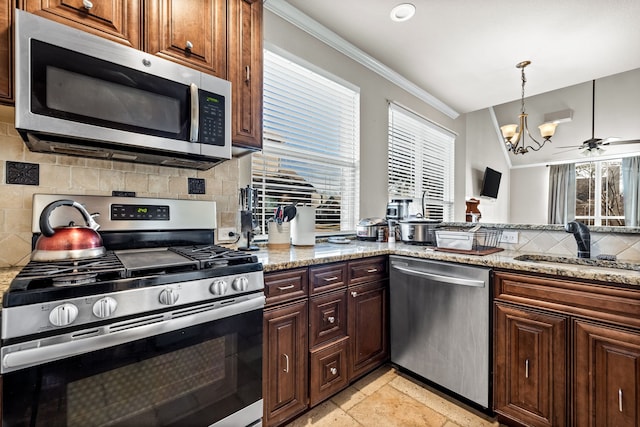 kitchen featuring ceiling fan with notable chandelier, a healthy amount of sunlight, light stone counters, and stainless steel appliances