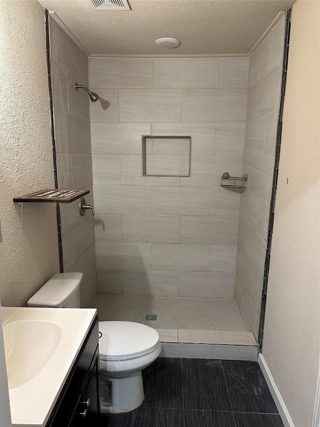 bathroom with vanity, a textured ceiling, tiled shower, and toilet