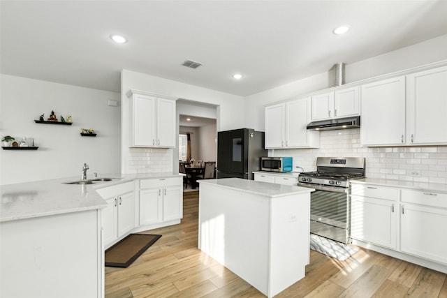 kitchen with kitchen peninsula, light stone counters, stainless steel appliances, sink, and white cabinetry