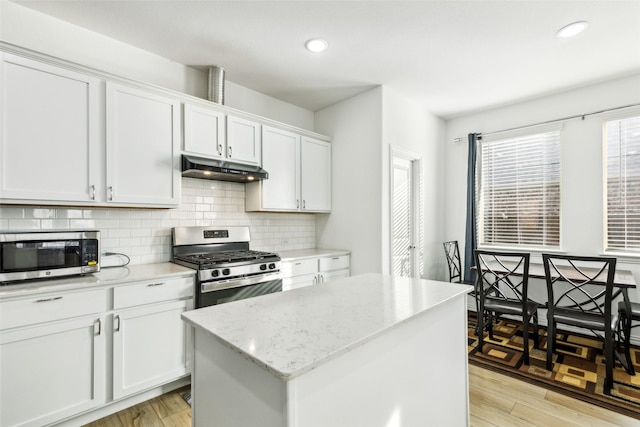 kitchen with light stone countertops, white cabinetry, stainless steel appliances, light hardwood / wood-style flooring, and a kitchen island