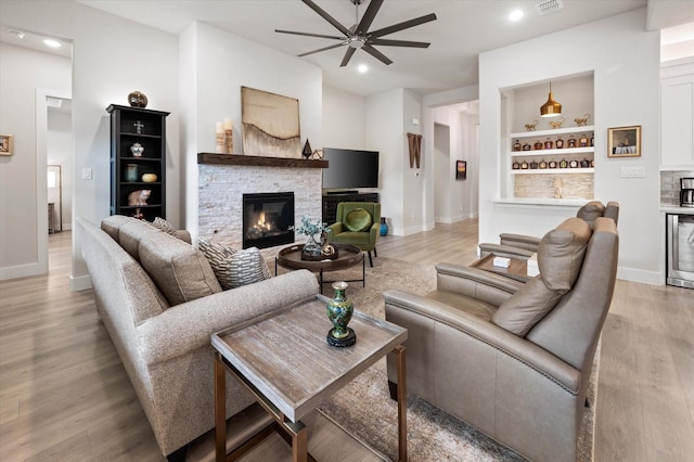 living room with beverage cooler, ceiling fan, built in features, a fireplace, and light hardwood / wood-style floors