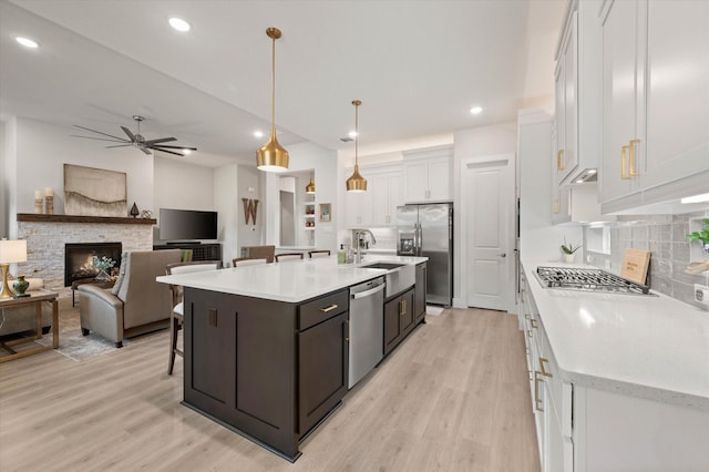 kitchen with hanging light fixtures, stainless steel appliances, backsplash, an island with sink, and white cabinets