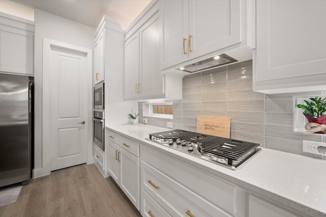 kitchen featuring light stone countertops, backsplash, stainless steel appliances, light hardwood / wood-style floors, and white cabinetry