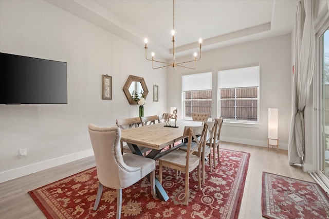 dining room featuring a raised ceiling, light wood-type flooring, and a chandelier