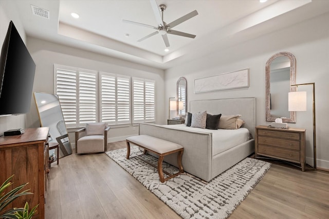 bedroom with a tray ceiling, ceiling fan, and light wood-type flooring