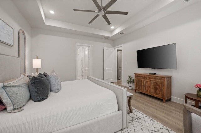 bedroom featuring ceiling fan, a raised ceiling, ensuite bath, and light hardwood / wood-style flooring