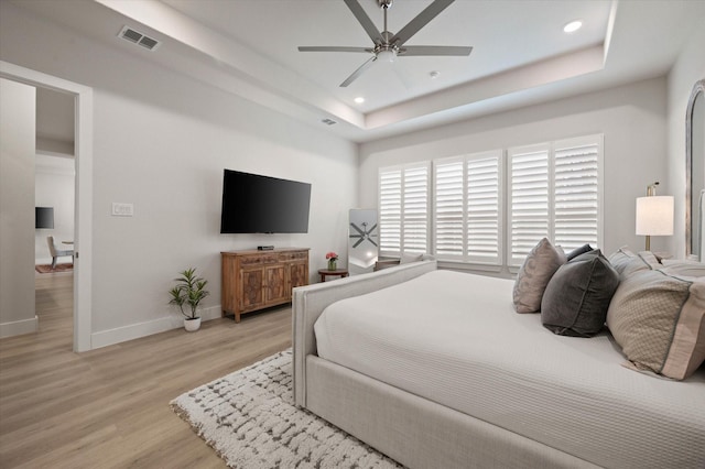 bedroom featuring light hardwood / wood-style floors, a raised ceiling, and ceiling fan