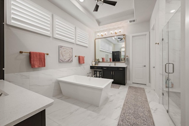 bathroom featuring ceiling fan, a raised ceiling, vanity, independent shower and bath, and tile walls