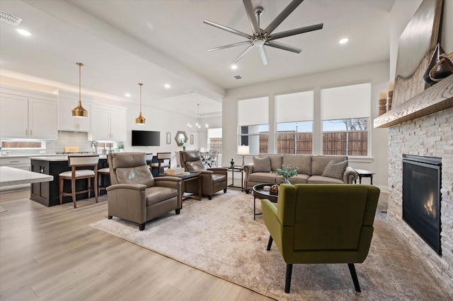 living room with ceiling fan with notable chandelier, light wood-type flooring, and a fireplace