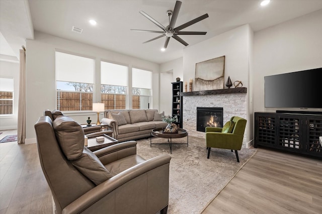 living room with light hardwood / wood-style floors, a stone fireplace, and ceiling fan